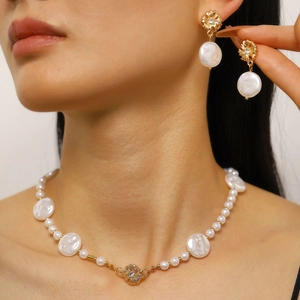 Dettaglio dell'elegante set di collana di perle barocche e orecchini a fiori dorati.
