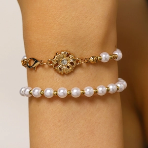 Dettaglio di un bracciale di perle con ciondolo a forma di fiore dorato indossato.