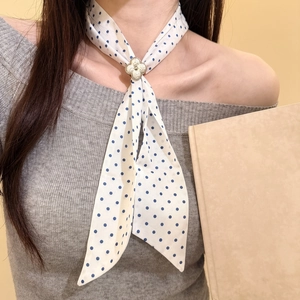Dettaglio di una collana sciarpa in seta bianca a pois blu con pendente a quadrifoglio