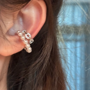 Close-up of elegant C-shaped ear cuff with pearls and zircons on ear.