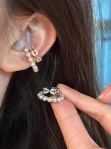 Detailed view of elegant pearl ear cuffs with crystal link design shown on ear and hand.