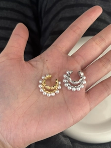 Close-up of elegant gold and silver tone pearl ear cuffs held in hand for size reference.