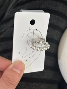 Detail of C-shaped ear cuff with white pearls and zircon crystals on display card.