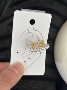 Close-up view of a gold-toned C-shaped ear cuff with white pearls and zircon bow detail.
