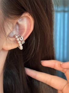 Macro view of elegant pearl and zircon C-shaped ear cuff jewelry worn on an ear
