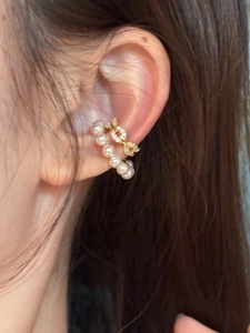 Detailed close-up of a delicate pearl ear clip and gold chain ear cuff on ear.