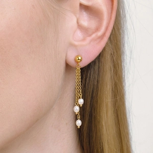 Detailopname van elegante gouden kwastjes oorbellen met zoetwaterparels aan het oor.