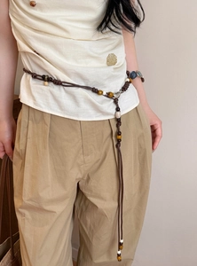Dettaglio catena in vita bohémien fatta a mano con perline marroni su pantaloni.