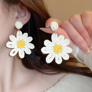 Macro view of elegant hand-woven white daisy flower drop earrings worn by a model