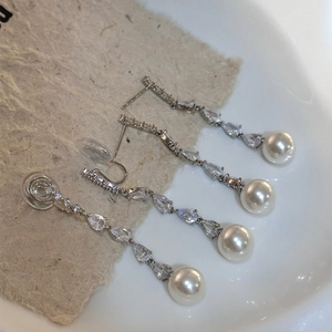 Detail of long zircon drop earrings with pearls, featuring both pierced and clip-on styles.