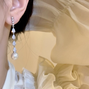Close-up shot of elegant long drop zircon earrings with a large white pearl bead on model ear.