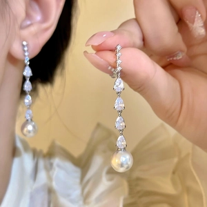 Close-up detail of elegant long drop earrings featuring pear-cut zircons and a white pearl