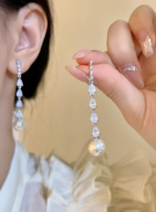 Close-up of elegant long dangle earrings featuring pear-shaped zircons and round pearls.
