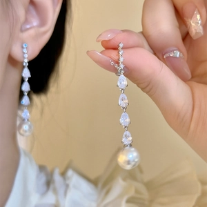 Detailed view of long dangling earrings featuring teardrop cubic zirconia and pearls