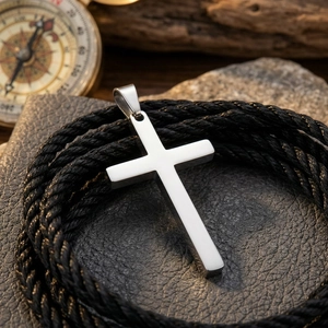 Macro view of a minimalist polished stainless steel cross pendant with black braided rope.