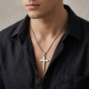 Close-up detail of a minimalist polished stainless steel cross pendant on a chain