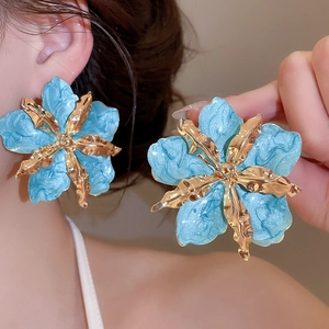 Primer plano de pendientes de flor azul esmaltada con detalles dorados