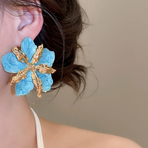 Primer plano detallado de arete de flor de esmalte azul exagerado con detalles de oro.