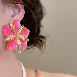 Primer plano de un pendiente de flor de esmalte rosa con bordes metálicos dorados