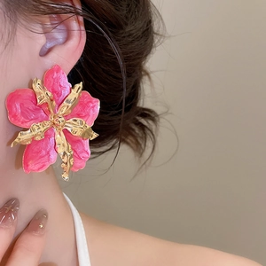 Primer plano de pendientes de flor esmaltada rosa con detalles metálicos dorados.