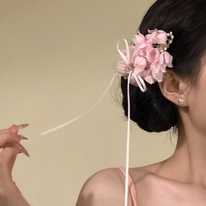Detail view of a pink floral hair clip with ribbons worn by a model in a soft aesthetic style.