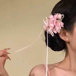 Side view of an elegant pink fabric flower hair clip with pearl accents and long ribbons