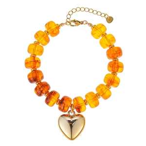 Detail van doorschijnende oranje harskralen en een grote gepolijste gouden hartvormige hanger.