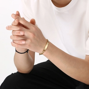 Close-up view of a minimalist gold-plated engravable ID plate bracelet on a model's wrist