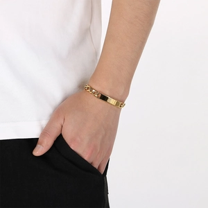 Close-up of minimalist gold curb chain bracelet with engravable ID plate on wrist.