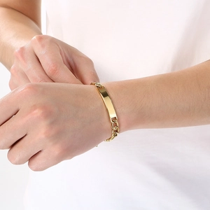 Close-up of a minimalist gold-toned polished ID curb chain bracelet on a wrist