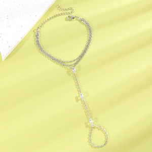 Détail d'un bracelet bague argenté avec zircons marquise sur fond vert clair.