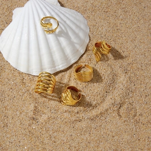 Collection of gold-toned stainless steel rings with wave and fish motifs on sand