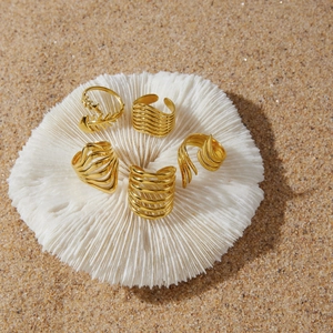 Detailed macro view of gold-toned stainless steel wave and fishbone rings on coral