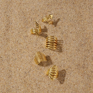 Detail view of five different gold fishbone and wave-themed rings on natural beach sand