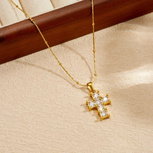 Dettaglio di una collana in acciaio inossidabile dorato con pendente a croce di cristallo.
