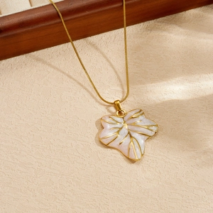 Primo piano della collana in acciaio dorato con dettaglio del pendente a foglia perlata.
