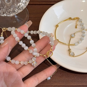 Close-up of elegant gold bracelets with white cat-eye beads and rhinestone charm.