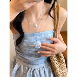 Detailopname van de vakantiestijl schelphanger ketting gedragen bij een blauwe zomerjurk