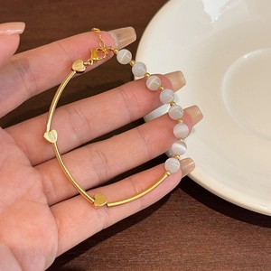 Macro view of gold heart charms and white cat eye stone beads on an adjustable bracelet