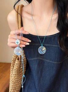 Detail view of ocean-themed necklace featuring real seashells in a blue resin pendant.