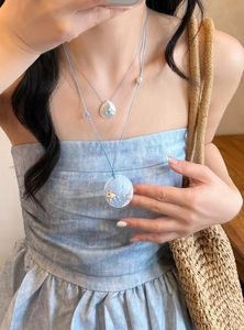 Detail of vacation style conch shell necklace with blue cord worn by model.