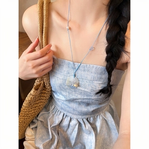 Summer style blue string pearl necklace worn by a female model with a woven bag