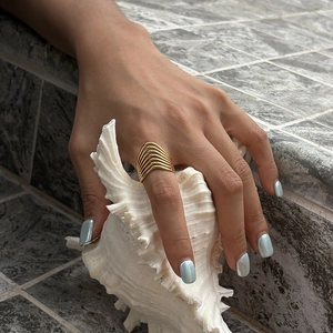 Detailed view of a multi-layer gold geometric ring on hand holding a white seashell