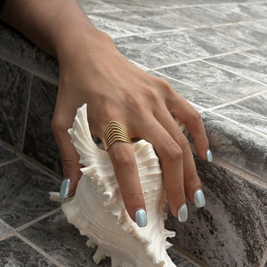 Elegant gold geometric multi-layer linear titanium steel ring shown on hand with conch shell.