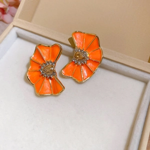 Detalle macro de pendientes de flores plisadas en esmalte naranja vibrante con pedrería