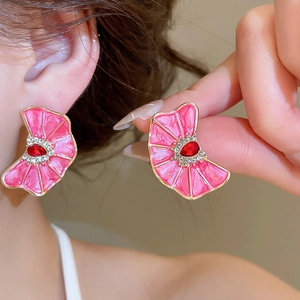 Primer plano de pendientes de flor de esmalte rosa con piedra roja y cristales
