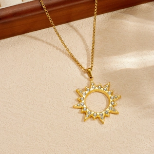 Dettaglio di una collana con pendente a sole dorato e cristalli scintillanti su beige.