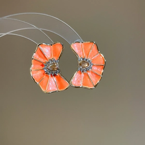 Primer plano de pendientes de flores naranjas con detalles de pedrería y gemas centrales