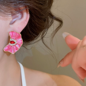 Primer plano de pendientes de flor plisada rosa con una gema roja en la oreja