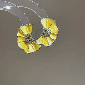 Primer plano de pendientes de flores de esmalte amarillo con detalles de pedrería.